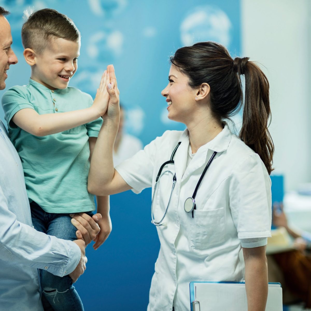 You’ve been really brave today! Happy female doctor giving high fie to a little boy who came with father at hospital.